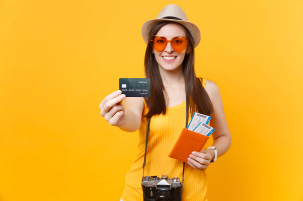 Heureuse femme touristique en vêtements décontractés d'été, chapeau tenant la carte de crédit, billets de passeport isolés sur fond jaune orange. Femme voyageant à l'étranger pour voyager le week-end escapade. Concept de vol aérien
 - Photo, image