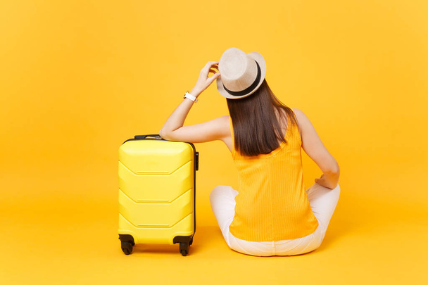 Utazó turisztikai nő nyári alkalmi ruha, kalap ülnek a bőröndöt, elszigetelt, a sárga-narancssárga háttérrel. Női utas utazik külföldre utazni, a menekülés hétvégén. Légi út fogalma - Fotó, kép