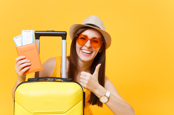 Viajante mulher turista em roupas casuais de verão, chapéu com mala mostrando polegar para cima isolado no fundo amarelo. Passageiro viajando para o exterior para viajar nos fins de semana de fuga. Conceito de viagem aérea
 - Foto, Imagem