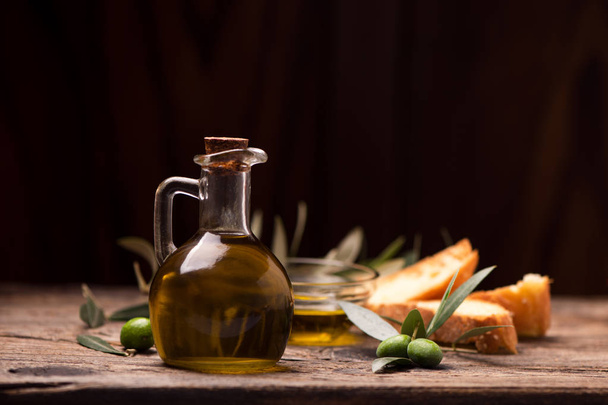 Olijfolie met brood op een houten tafel. Rustieke vintage samenstelling - Foto, afbeelding