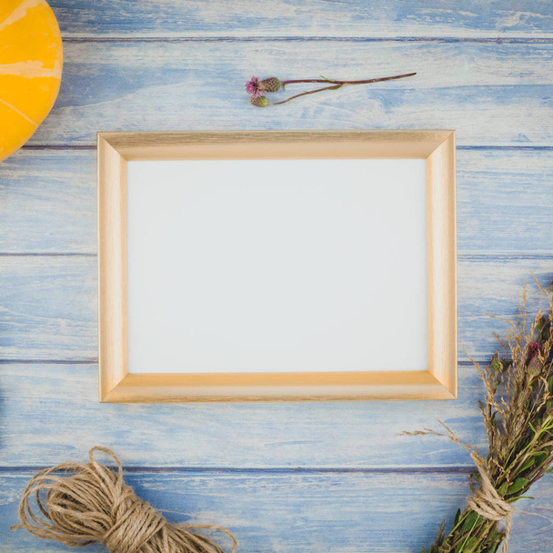 Τετράγωνη κάτοψη του φθινοπώρου πορτοκαλί κολοκύθες και ξηρά λουλούδια με χόρτο Ευχαριστιών φόντο πάνω από μπλε τονισμένο ξύλινο τραπέζι με Χρυσή κορνίζα mock και να αντιγράψετε το χώρο σε ρουστίκ στυλ, πρότυπο για το κείμενο - Φωτογραφία, εικόνα