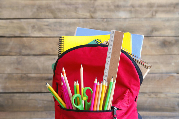Rucksack mit Schulmaterial auf Holztisch - Foto, Bild