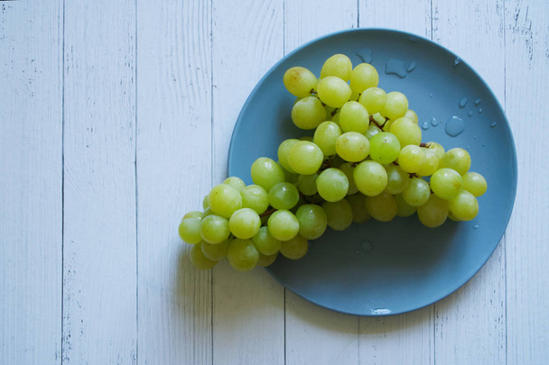 White grapes lie in a blue plate on a light natural background.                                - Valokuva, kuva