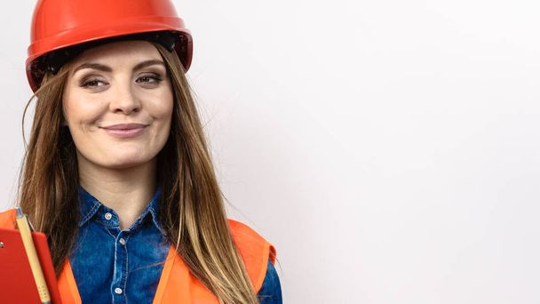 Woman construction worker builder structural engineerin in orange vest red hard helmet holds pen file pad. Safety in industrial work. Studio shot - Foto, Imagem