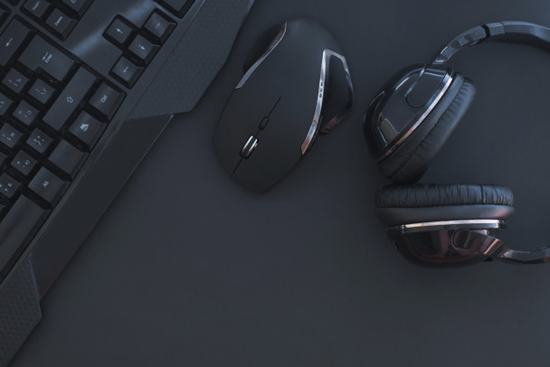 Zwarte muis, het toetsenbord, de hoofdtelefoons worden geïsoleerd op een donkere achtergrond, het bovenaanzicht. Plat lag gamer achtergrond. Werkplek met een toetsenbord, muis en koptelefoon op een zwarte achtergrond. Copyspace - Foto, afbeelding