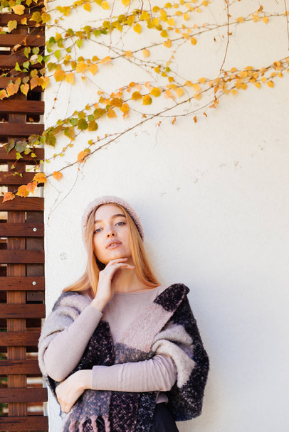 young blue-eyed girl blonde in warm stylish clothes posing against wall in a shot in the sun - Foto, afbeelding
