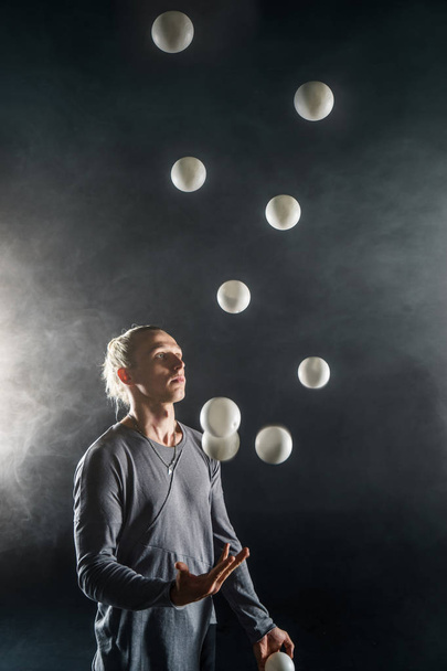 Blond jongleur met witte ballen op zwarte achtergrond - Foto, afbeelding