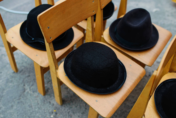 Πολλά μαύρα καπέλα ρετρό βρίσκονται στις ξύλινες καρέκλες. - Φωτογραφία, εικόνα