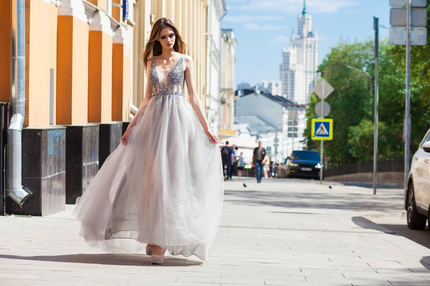 Young beautiful brunette woman in white flowers dress walking on the street, summer outdoors - Фото, зображення