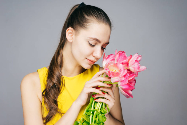 cute pretty girl in a yellow dress holding a bouquet of pink flowers in her hands, enjoying the scent - Photo, Image