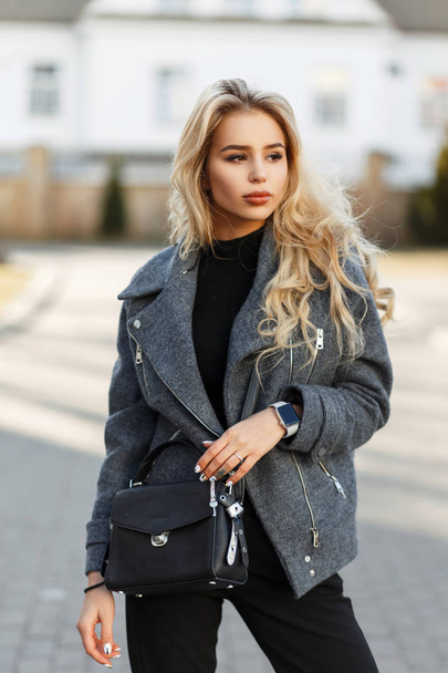 Fashion young model woman with a stylish black handbag in a fashionable spring coat on a sunny day - Foto, Imagem