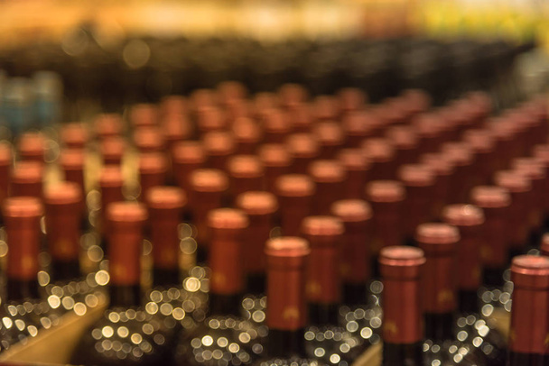 Gruppo di bottiglie di vino rosso sfocate e ravvicinate in cantina nella sezione vini del moderno magazzino di distribuzione. Inventario, logistica, affari, commercio all'ingrosso, concetto di esportazione. Bevande alcoliche
. - Foto, immagini