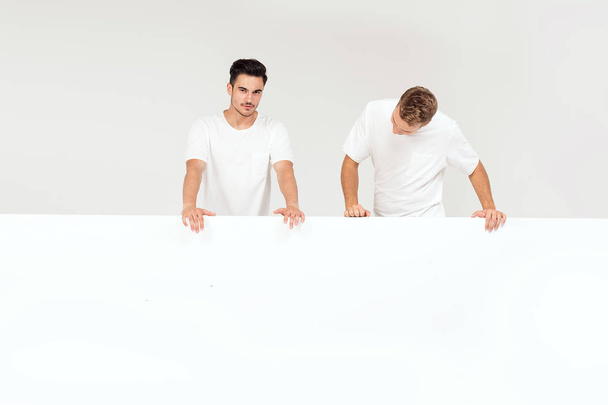 Due giovani bei ragazzi in possesso di banner bianco vuoto, cartello, isolato su sfondo bianco studio
. - Foto, immagini