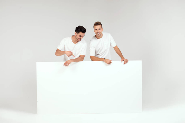 Two young handsome guys holding blank white banner, signboard, isolated on white studio background. - Foto, immagini