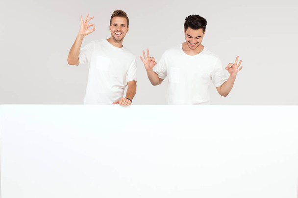Two young handsome guys holding blank white banner, signboard, isolated on white studio background. - Photo, Image