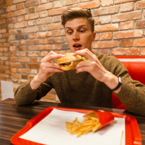 Young guy with a hamburger in a restaurant. Surprised emotion - Foto, afbeelding