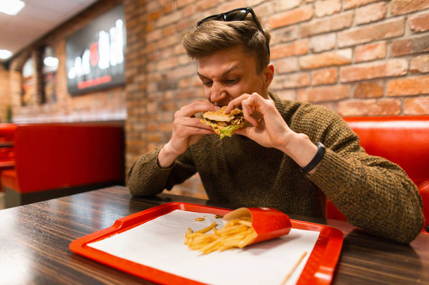 hipster man with a hamburger and french fries in a restaurant - Valokuva, kuva