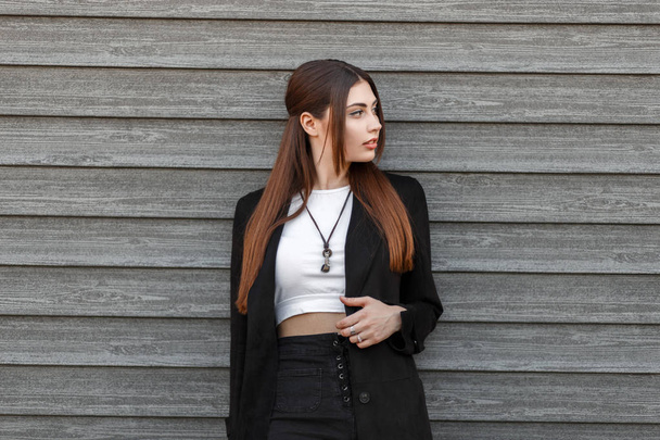 Tyylikäs kaunis nuori nainen muoti musta takki seisoo lähellä puinen seinä kadulla
 - Valokuva, kuva