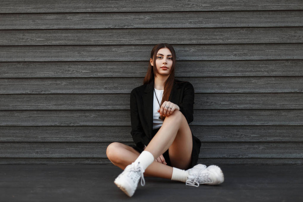 Krásná mladá žena v módní oblečení sedí poblíž dřevěné stěny - Fotografie, Obrázek