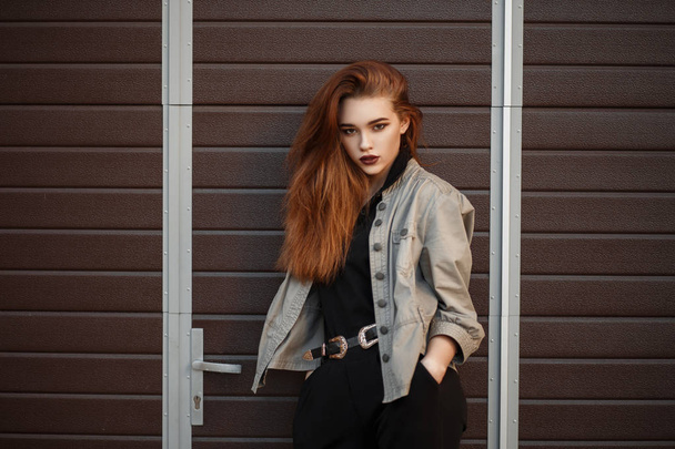 Beautiful young model girl in stylish jacket and black polo shirt posing near the gate - Fotoğraf, Görsel