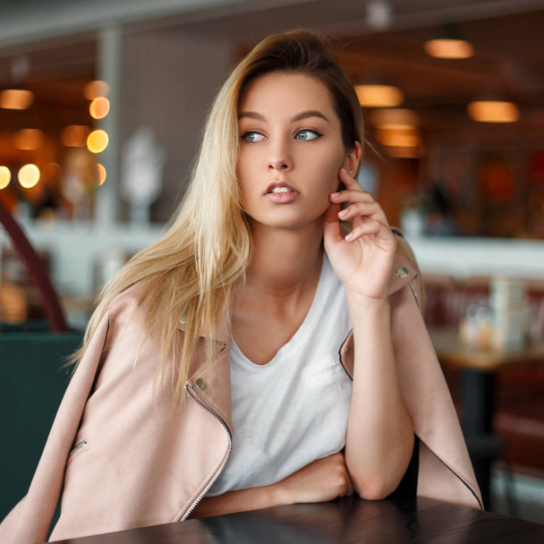 Elegante hermosa mujer joven con una chaqueta rosa y una camiseta blanca sentada en un restaurante
 - Foto, Imagen