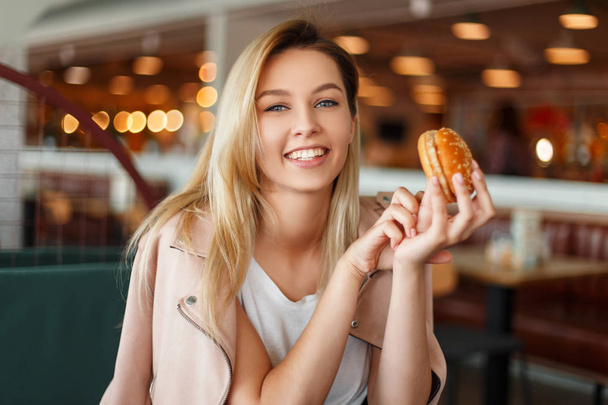 Krásná mladá žena v módní růžové sako s hamburger v kavárně - Fotografie, Obrázek