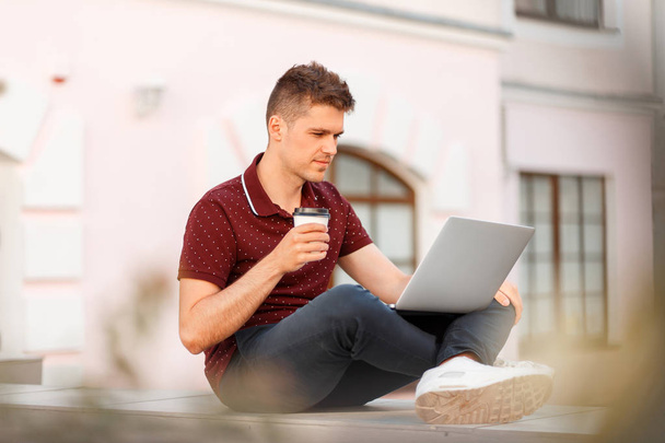 Young businessman blogger man drinks coffee and works on a laptop in the city - Photo, Image