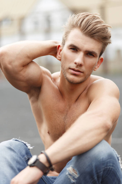 Όμορφος μοντέρνος γυμναστήριο μοντέλο άνθρωπος με ένα χτένισμα με ένα υγιές σώμα, κάθεται στο δρόμο - Φωτογραφία, εικόνα