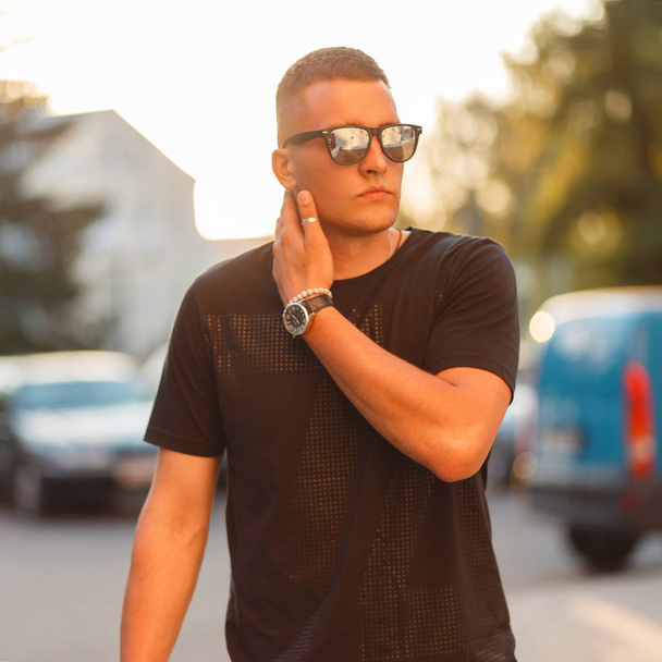Hipster człowiek z fryzura w stylowych okularów przeciwsłonecznych i czarny moda T-shirt o zachodzie słońca - Zdjęcie, obraz