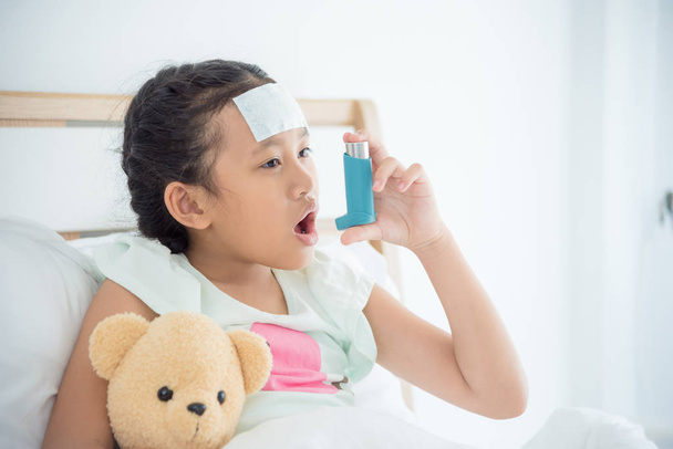 Young asian girl sitting on bed and using broncodilator inhaler for relieve asthma symptom - Photo, Image