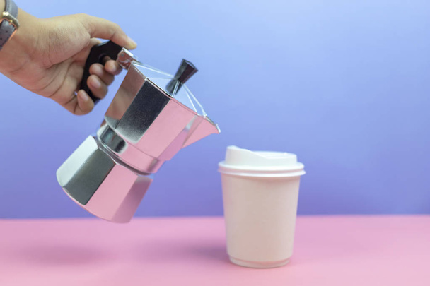 mão segurando máquina de café expresso derramando café em copo de papel com fundo pastel
. - Foto, Imagem
