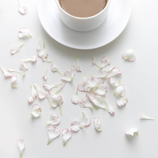 A white cup of coffee with carnation petals on white background. flat lay. Top view. - Foto, Imagem