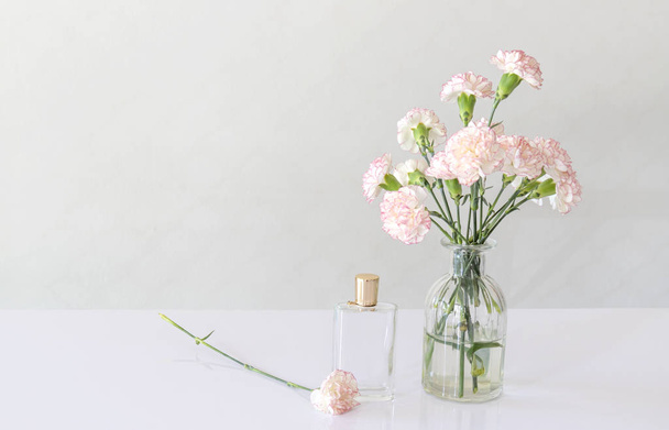 botella de perfume con florero de flores de clavel en la mesa blanca
. - Foto, Imagen