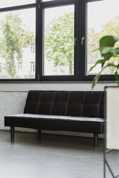 άδειο μοντέρνο μαύρο καναπέ κοντά στο παράθυρο στο σύγχρονο γραφείο - Φωτογραφία, εικόνα