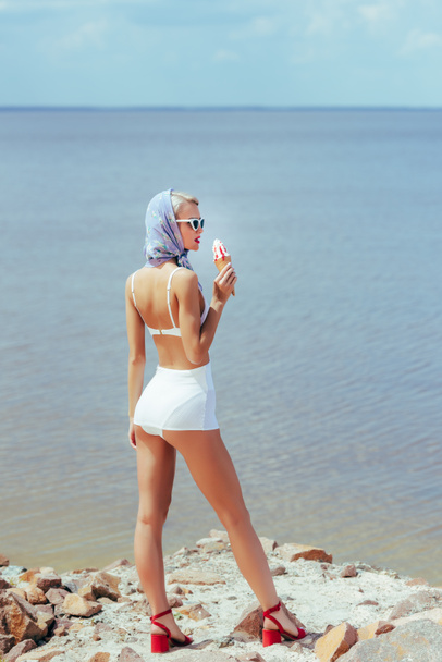 back view of elegant woman in vintage swimsuit holding ice cream and posing at sea - Photo, Image