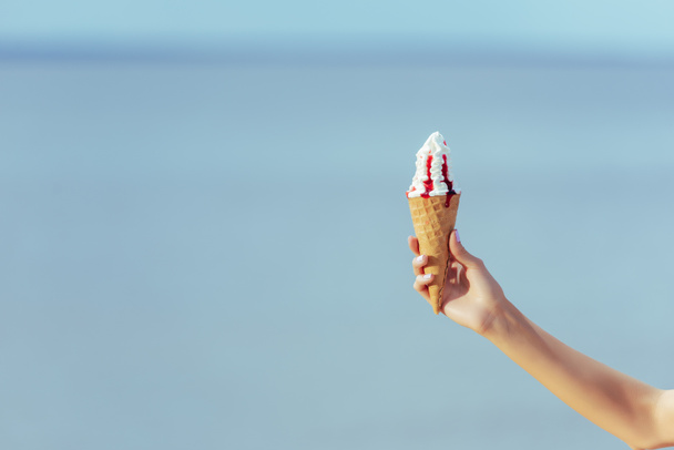 vista parcial de la mujer sosteniendo cono de gofre con helado dulce en la mano
 - Foto, imagen
