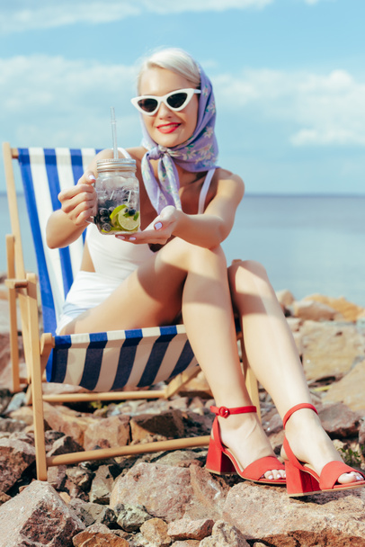 beautiful smiling girl holding lemonade in mason jar and resting in beach chair - Foto, imagen