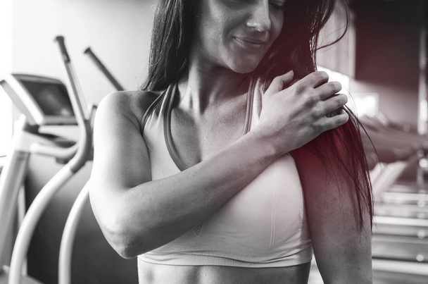 Black and white photo of beautiful young woman holding her arms, feeling pain during workout. - Photo, image