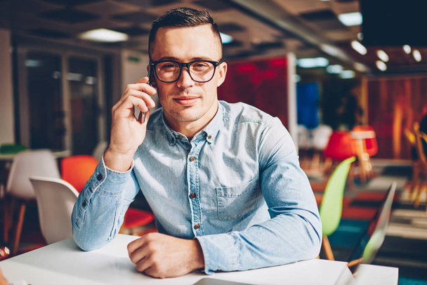 Portrait of professional male manager satisfied with mobile tariffs making phone calls on work,young businessman in eyewear looking at camera during telephone conversation with banking service operator - Photo, image