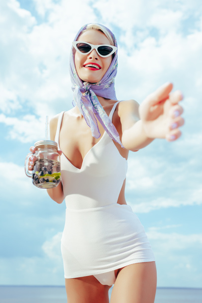 白いビンテージ水着で身振りで示すことと新鮮な飲み物と石工の瓶を保持している美しい幸せな女の選択と集中 - 写真・画像
