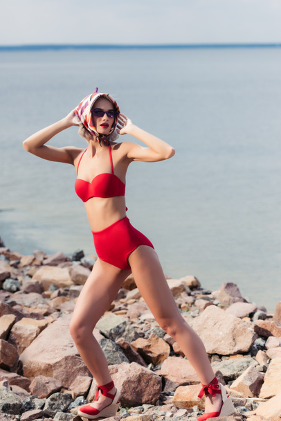 jolie fille élégante posant en écharpe de soie et bikini rouge vintage sur la plage rocheuse
 - Photo, image