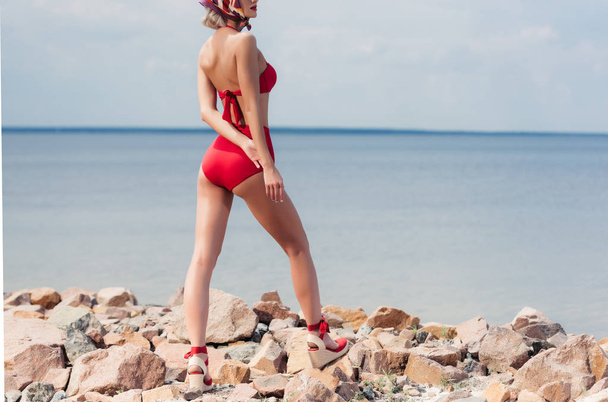 przycięte widzenia modne dziewczyna pozuje w czerwonym bikini na kamienistej plaży - Zdjęcie, obraz