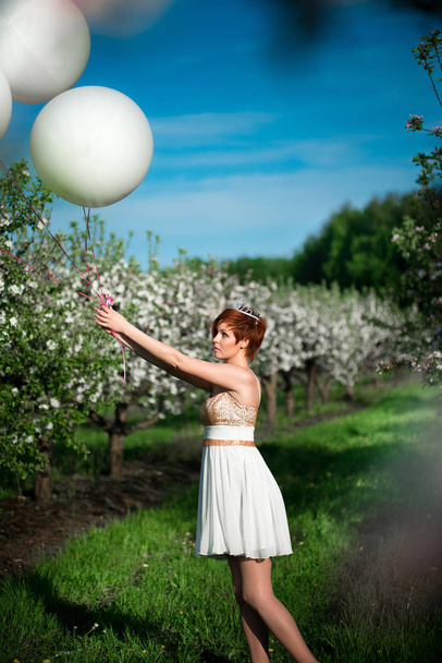 Okouzlující dívka drží bílé balóny, bohužel při pohledu na ně, nechat je jít. Kvetoucí zahrady a jarní obloze na pozadí - Fotografie, Obrázek