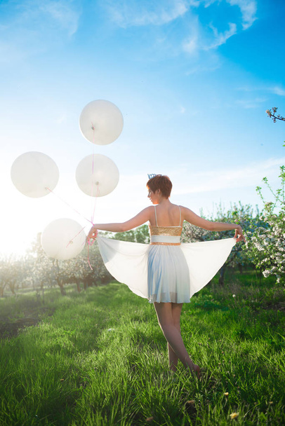 Chica vestida blanca caminando en un jardín verde con enormes globos de aire blanco, su espalda a nosotros
 - Foto, imagen