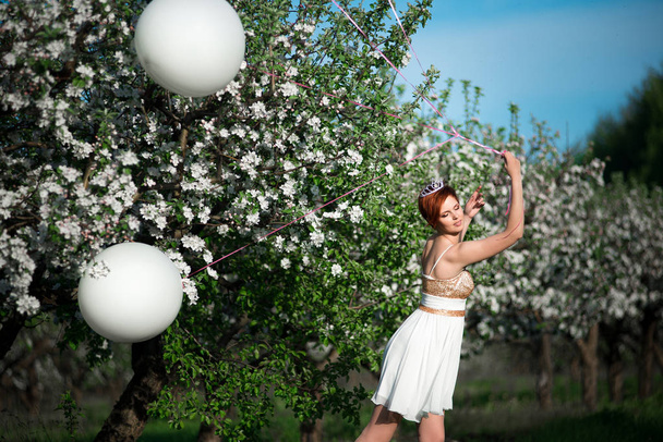 Chica juguetona sostiene los globos y en un día cálido y soleado en el jardín de manzanas
 - Foto, imagen