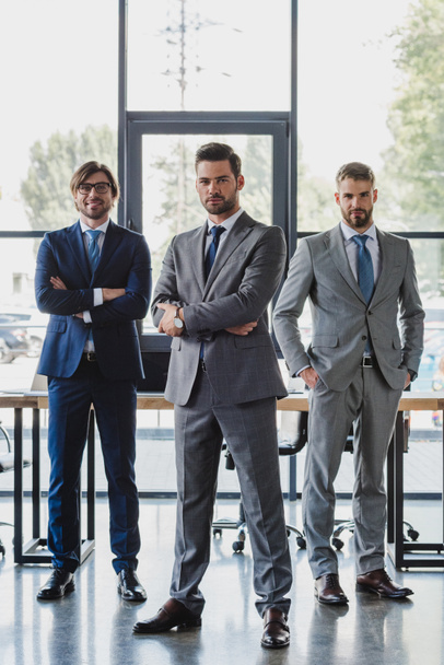 Selbstbewusste junge Geschäftsleute in formaler Kleidung stehen zusammen und blicken im Büro in die Kamera - Foto, Bild