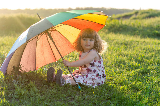 Beautiful girl plays on nature with a colorful umbrella. Rainbow umbrella in the hands of the child - Photo, Image