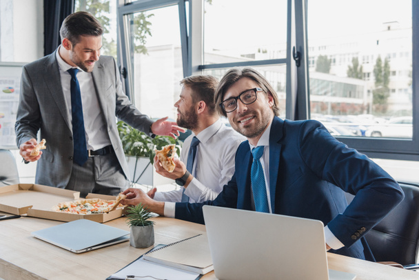 jóvenes empresarios sonrientes comiendo pizza en el lugar de trabajo
  - Foto, imagen