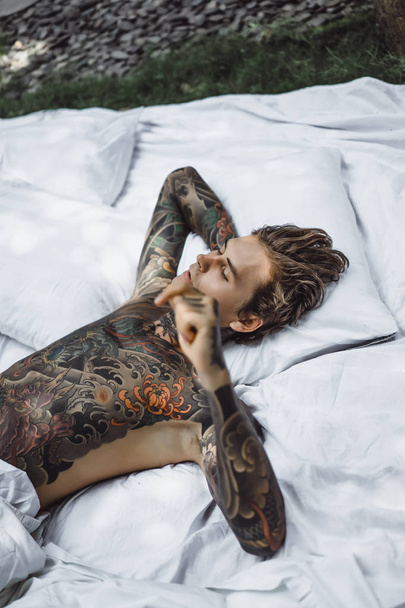 Handsome young tattooed man relaxing on white bed - Foto, afbeelding
