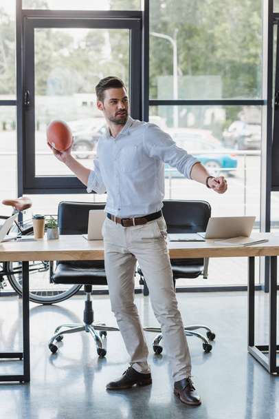 όμορφος νέος επιχειρηματίας που παίζει με τη μπάλα του ράγκμπι στο γραφείο - Φωτογραφία, εικόνα